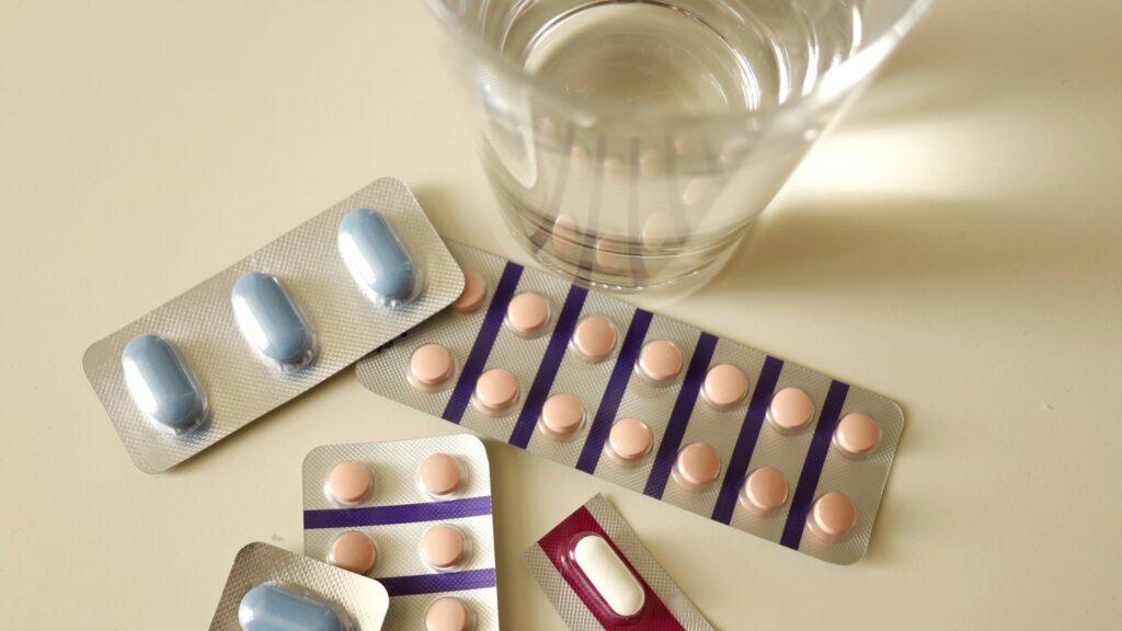 薬剤師の将来性に関わる適切な服薬管理をイメージさせる、瓶から出た錠剤と飲み水のコップ。