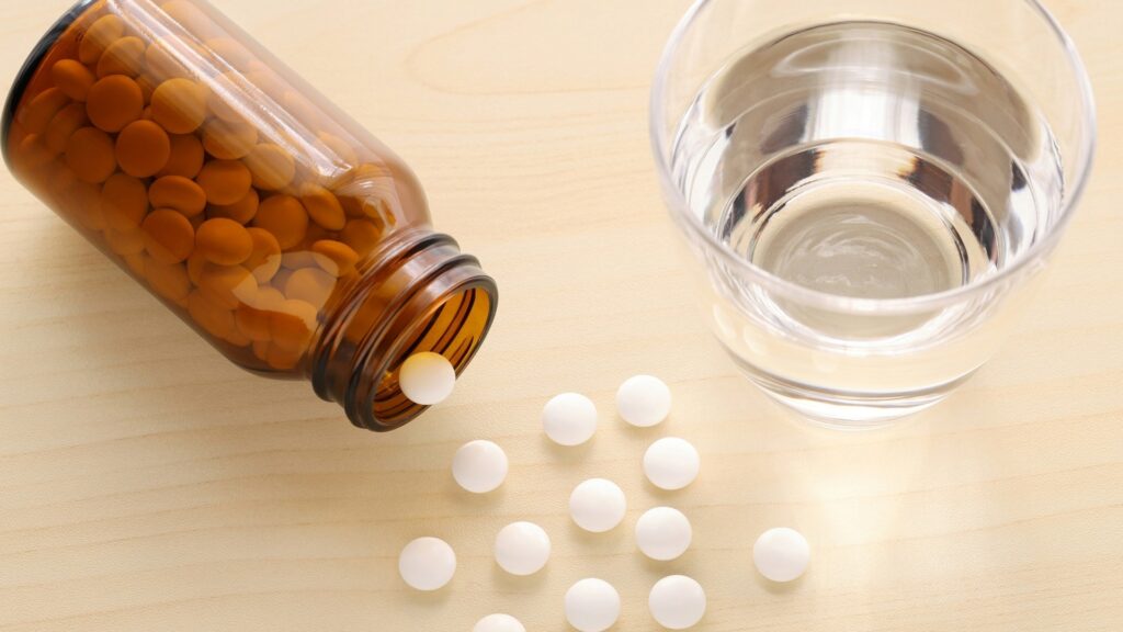 薬剤師の将来性に関わる適切な服薬管理をイメージさせる、瓶から出た錠剤と飲み水のコップ。